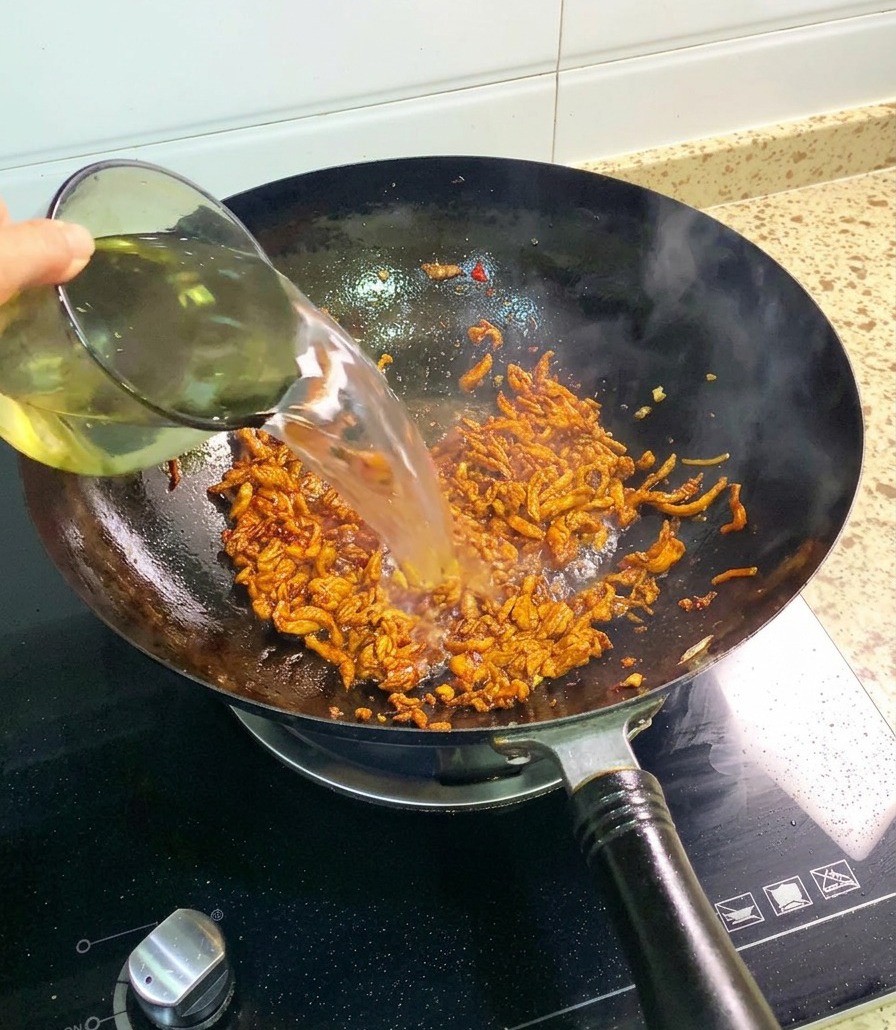 調味料が絡んだ鶏肉の千切りが入った中華鍋に、グラスから透き通った水を注ぎ入れる様子。
