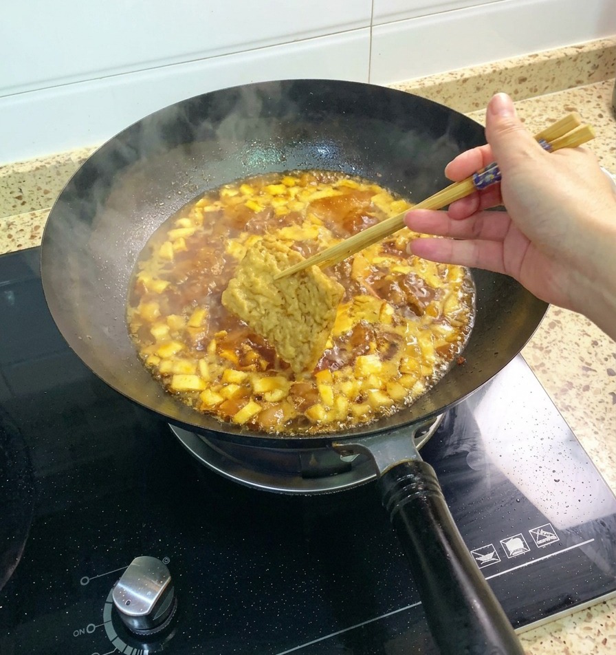 箸で持った厚揚げを、グツグツと泡立つ鶏肉としいたけのソースに浸している様子。
