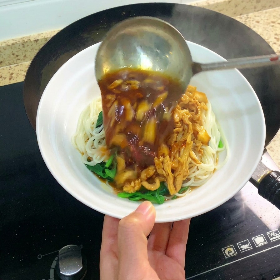 白い器に盛られた麺の上に、大きな金属製のレードルで具沢山の濃厚な鶏肉ソースをかけている様子。