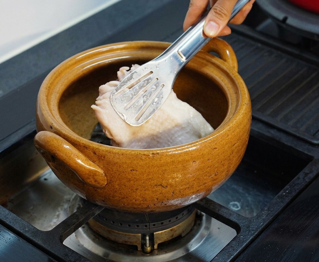 湯通しした鶏もも肉を、昆布の入った茶色い土鍋の中にトングで入れている様子。