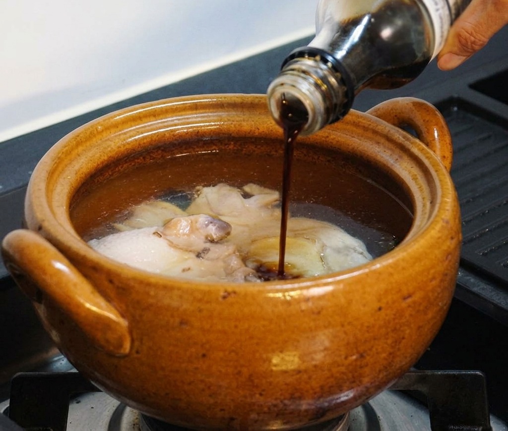 鶏肉と水が入った鍋に、ガラス瓶から醤油を注ぎ入れている様子。