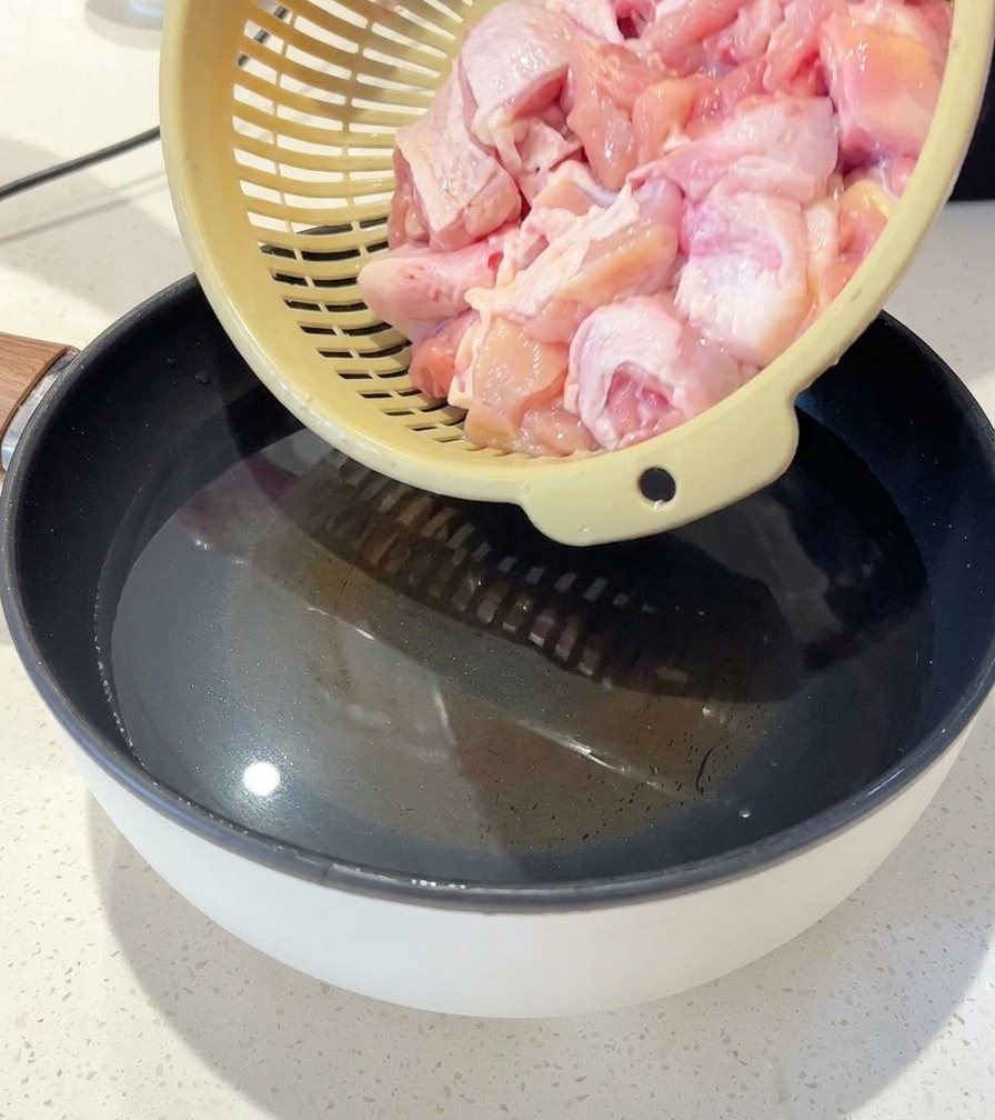 スライスした生姜と青ねぎが入った鍋の水に、ザルから生の鶏肉を入れようとしている様子。