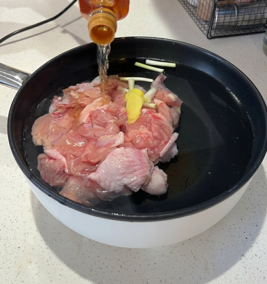ガラス瓶から、鶏肉と香味野菜が入った鍋の水に透明な琥珀色の液体を注いでいる様子。