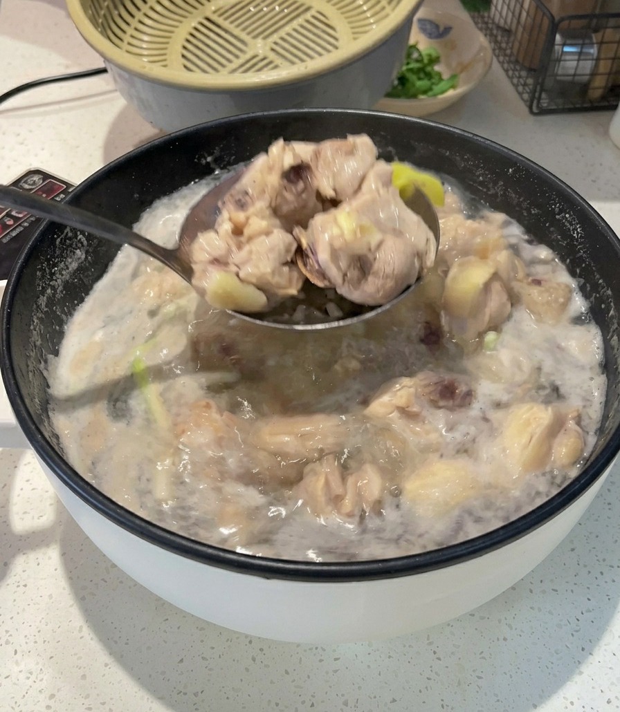 泡立つ沸騰したお湯が残る鍋から、下茹でされて白っぽくなった鶏肉の切れ端を穴あきお玉で丁寧にすくい上げている様子。