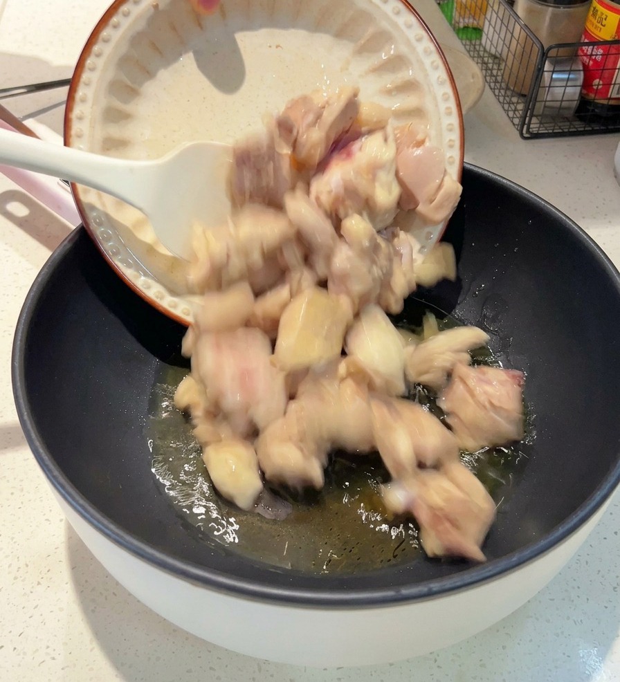 油が温まり、うっすらと光る黒いフライパンに、白いお皿から下茹でした鶏肉を移し入れている様子。