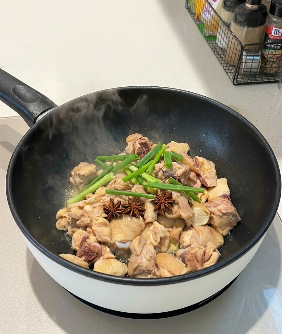 湯気が上がるフライパンの中で、鶏肉の上に丸ごとの八角とカットした青ねぎが添えられている様子。