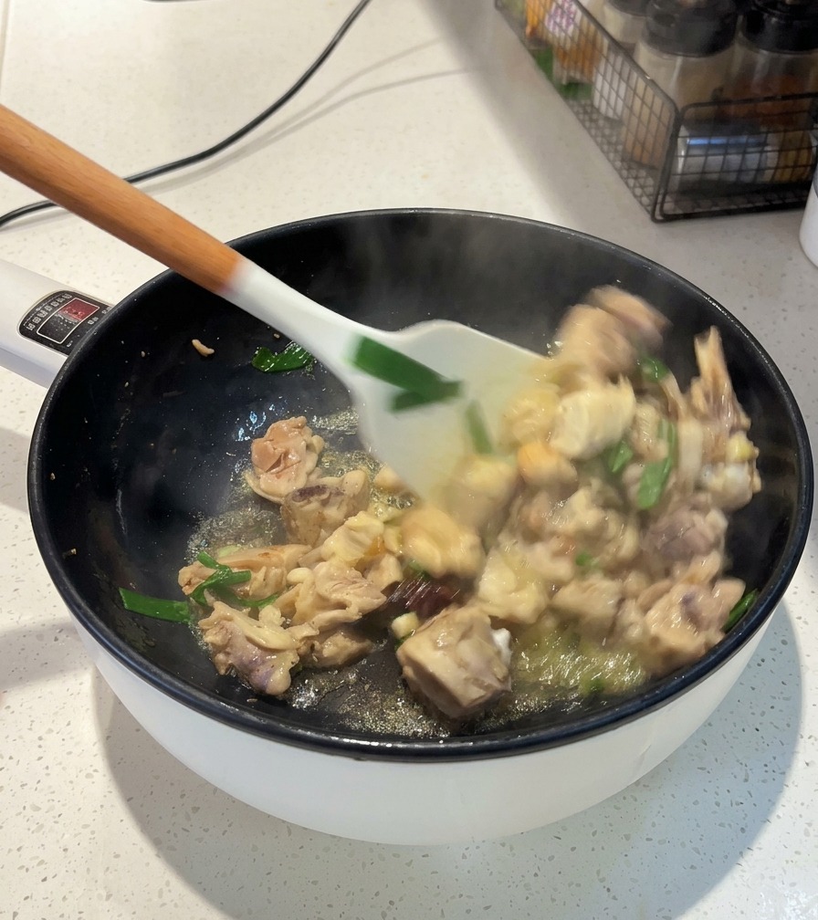 白いヘラを使い、加熱中のフライパンで鶏肉、青ねぎ、八角を混ぜ合わせながら炒めている様子。