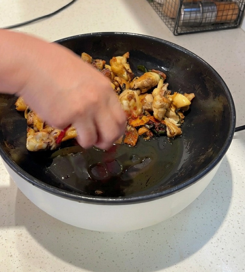 焼き色のついた鶏肉が入った黒いフライパンに、丸ごとの乾燥赤唐辛子と鮮やかな赤色の粉唐辛子を加えて炒めている様子。