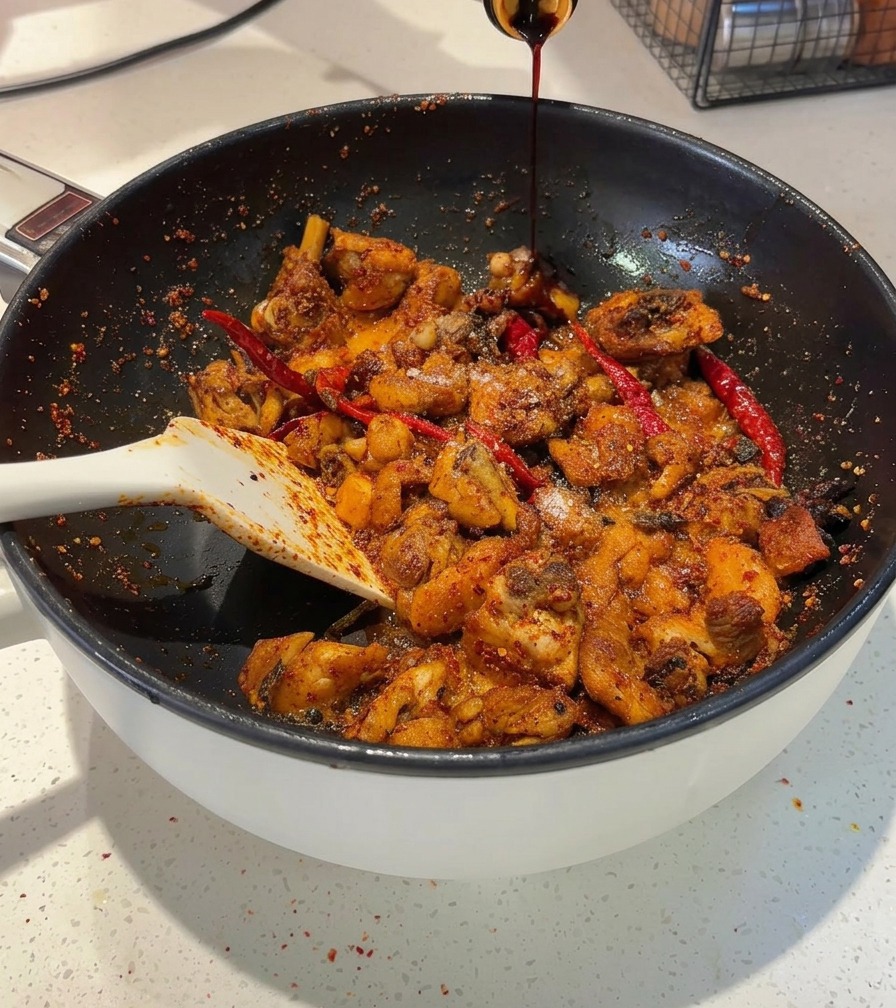 ピリ辛に炒めた鶏肉が入ったフライパンに、ボトルから中国たまり醤油を注ぎ入れている様子。