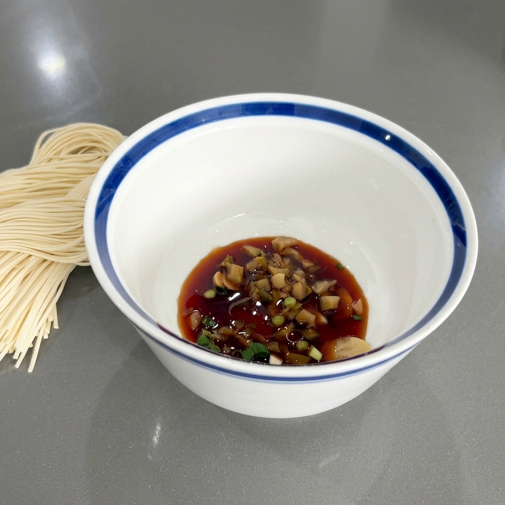 醤油やねぎ、薬味が入ったどんぶりの表面に、加えたてのごま油が綺麗な艶を作っている様子。