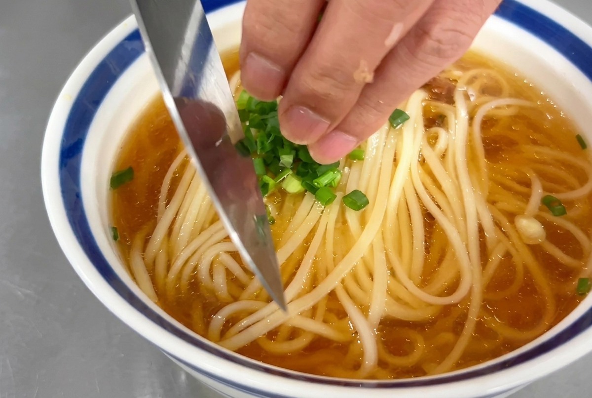 ラーメンの器の中央に、手元で刻んだ輪切りの青ねぎをパラパラと散らしている様子。