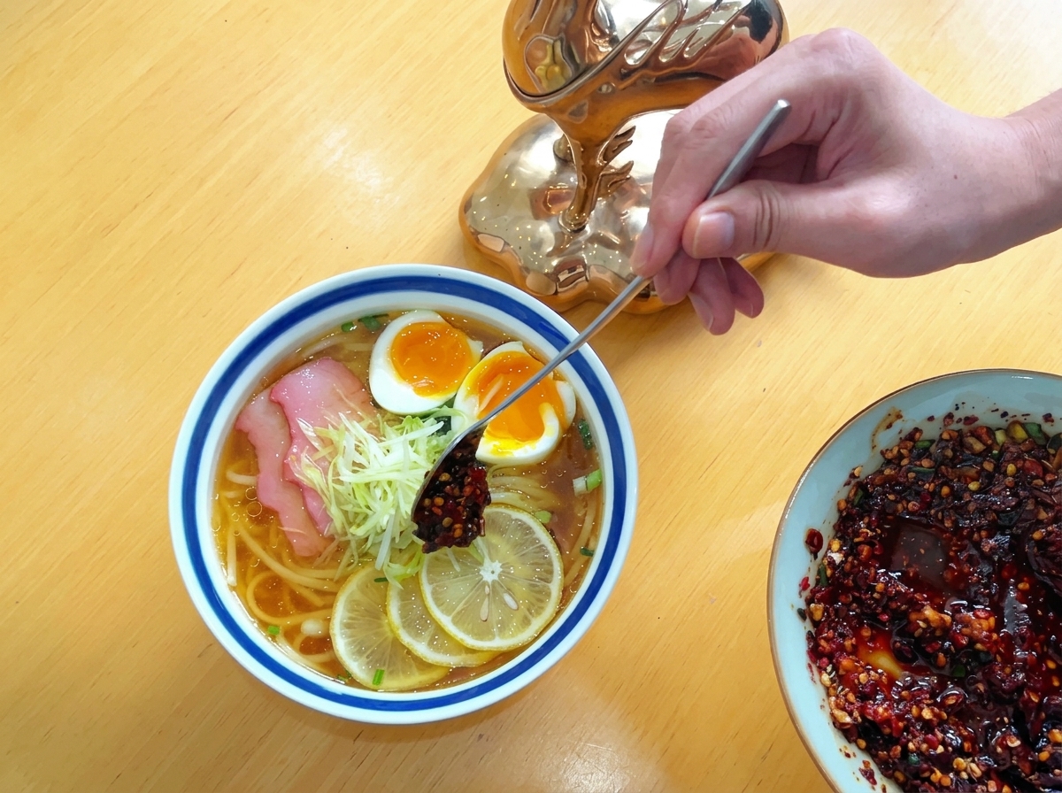 長い金属製のスプーンを使い、ラーメンの器に盛られた大根の千切りの上に、深紅のラー油を少し乗せている様子。