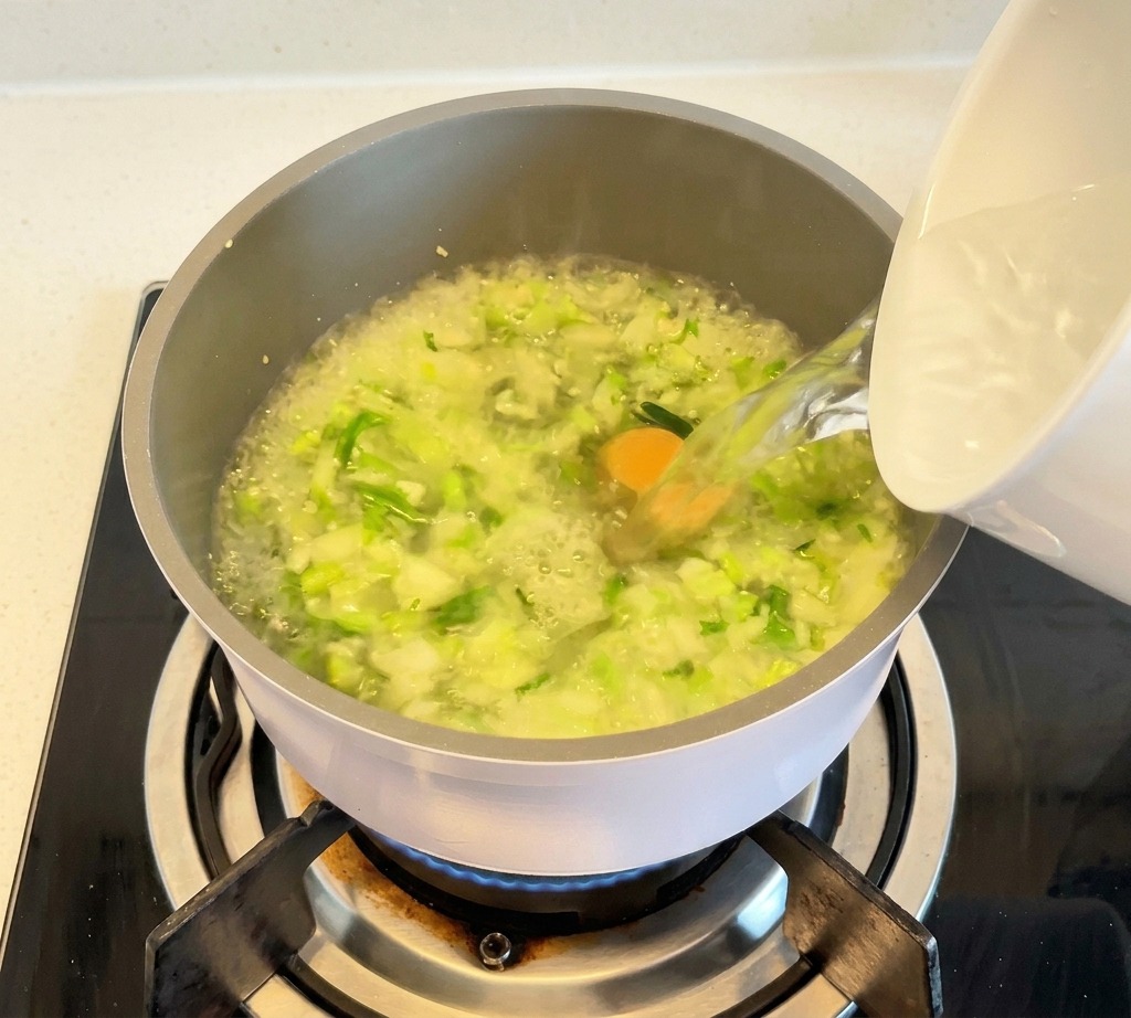 野菜と澄んだスープが入った鍋に、白い器から熱湯を注ぎ入れている様子。