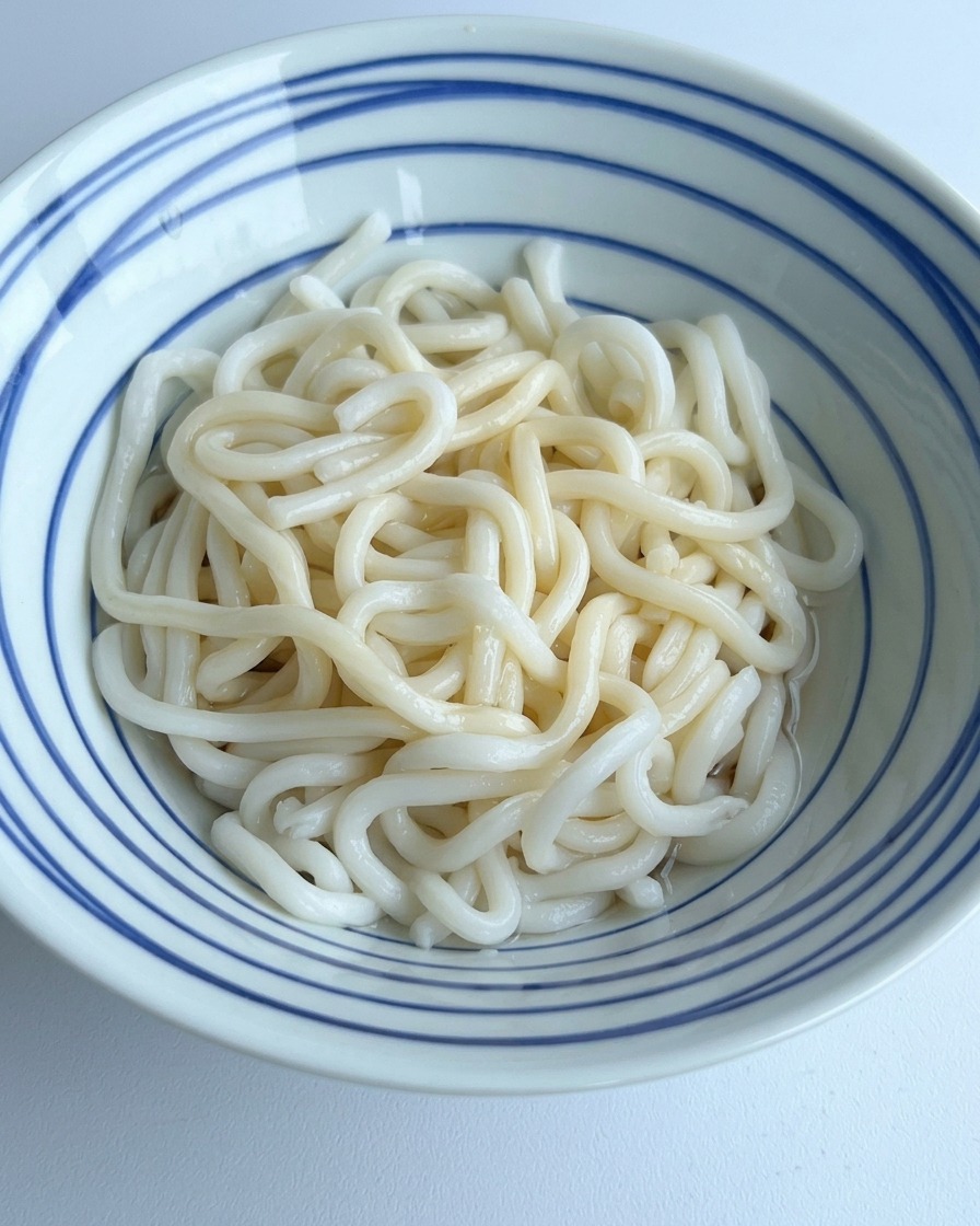 器の底にある濃い調味料と混ざり合うように、うどんの入った器に澄んだお水を注いでいる様子。