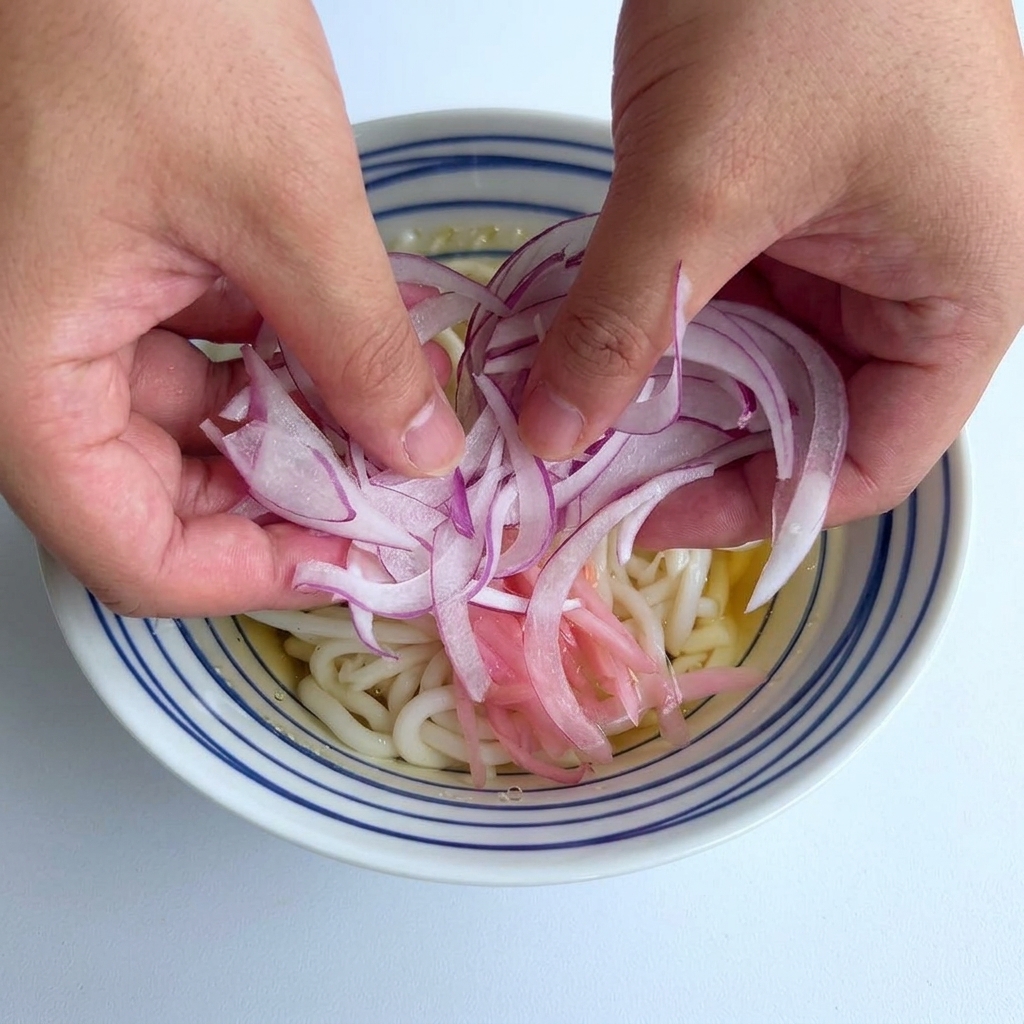うどんの器の中央に、両手で薄切りにした紫赤色の玉ねぎをたっぷりのせている様子。