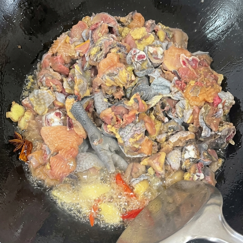 中華鍋の中で烏骨鶏のぶつ切りがスパイスと共に豪快に炒められ、油が泡立ち味が馴染んでいくクローズアップ。