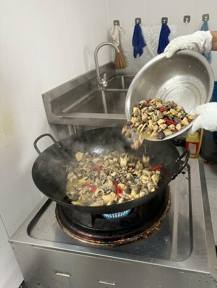 焼き色がついた鶏肉とスパイスが入った湯気立つ中華鍋に、容器から透明な熱湯を注ぎ入れている様子。