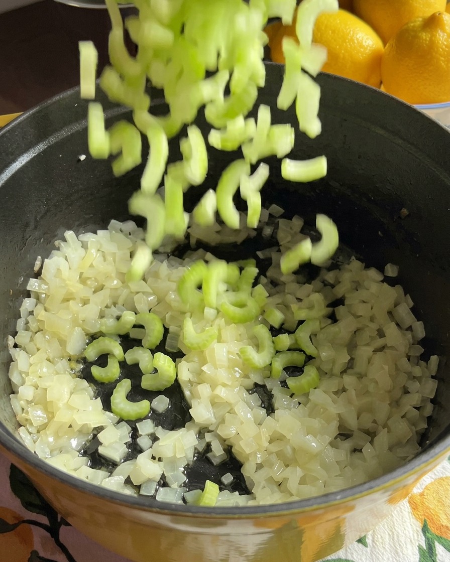 玉ねぎとにんじんの輪切りが入った調理鍋に、刻んだ緑色のセロリが投入されている様子。