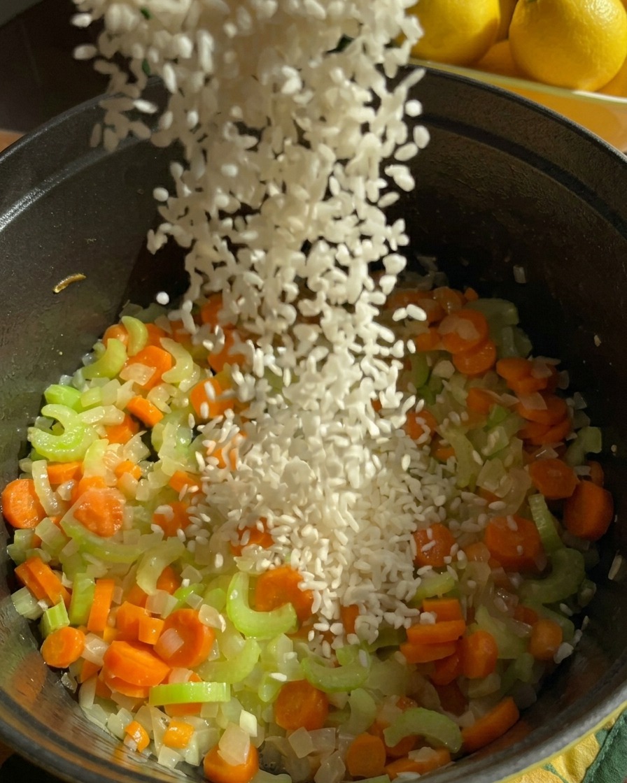 炒めたにんじん、セロリ、玉ねぎが入った黒い鍋に、白いジャスミンライスが注がれている様子。