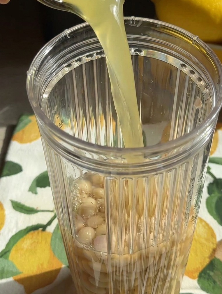 丸ごとの白いんげん豆が入ったミキサーのカップに、グラスから薄黄色の液体が注がれている様子。
