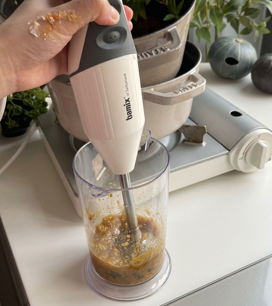 滑らかなオレンジ色のかぼちゃスープの鍋に、白いココナッツミルクを回しかけ、スパチュラで混ぜ合わせている様子。