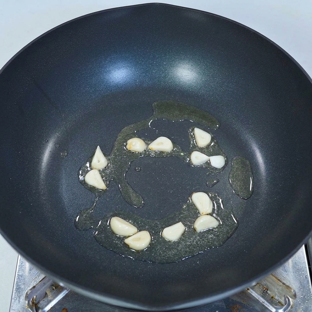 黒い中華鍋の底に引かれた少量の油の中で、薄切りにしたにんにくがパチパチと音を立てて炒められている様子。