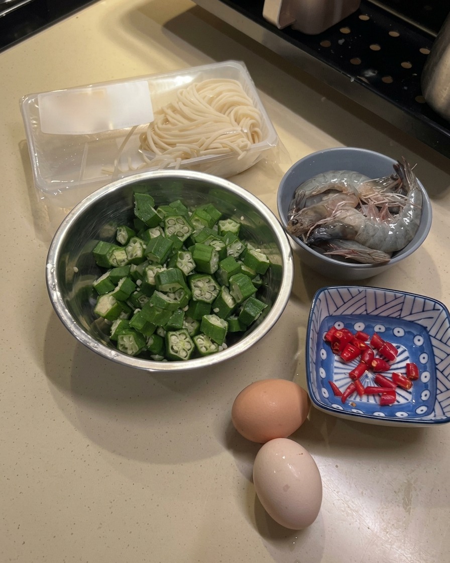 まな板の上に用意された新鮮なオクラ、生エビ、卵2個、中華麺。