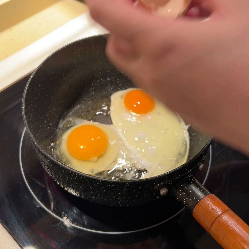 黒いフライパンで焼かれている2つの目玉焼き。