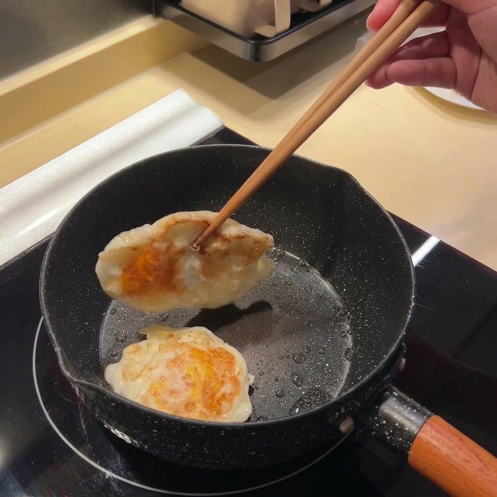 縁がこんがりと焼けた目玉焼きを、フライパンの中で菜箸を使って裏返している様子。