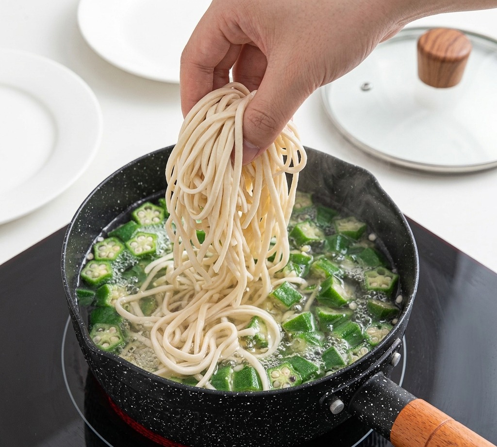 沸騰したオクラ入りの鍋に、白い生麺を入れている様子。