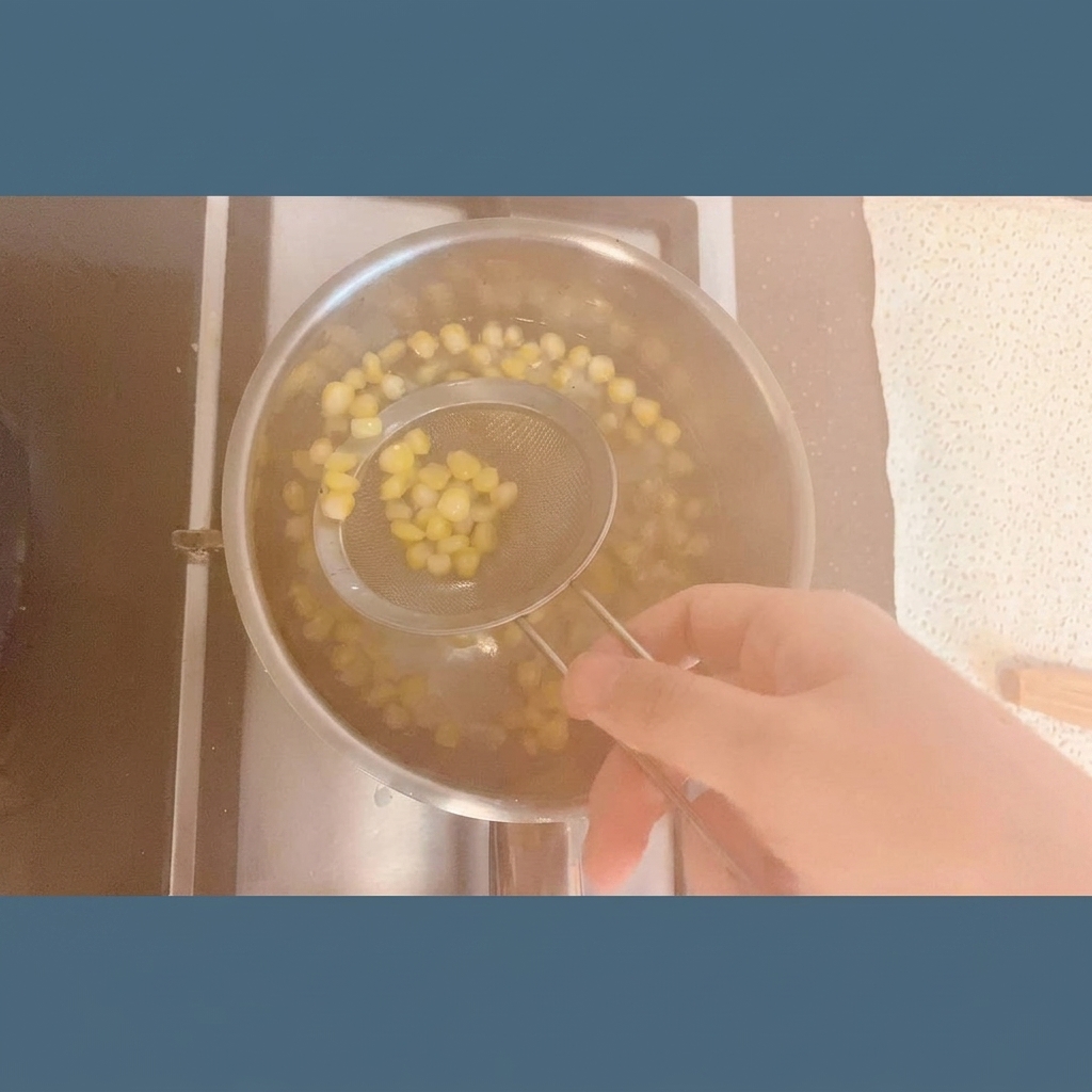 湯気が立つ鍋から、ステンレス製の網じゃくしで引き上げられる鮮やかな黄色のコーン粒。