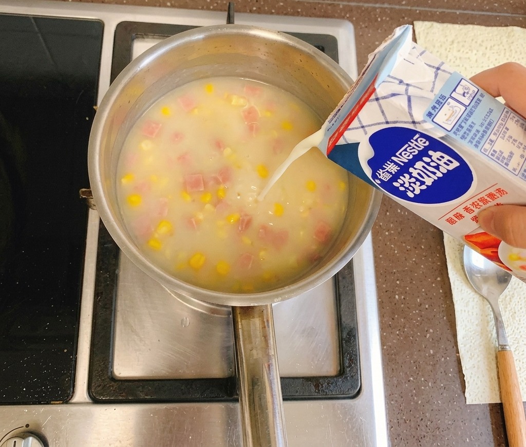 コンロの上で煮立つクリーミーなコーンスープの鍋に、青と白のパックから注がれる生クリーム。