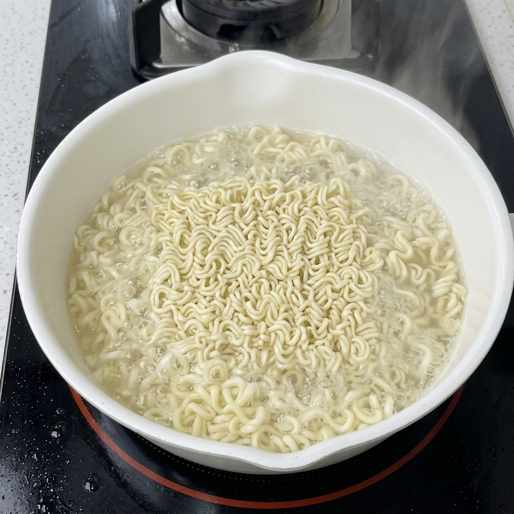 コンロの上の白い鍋で、2個のインスタントラーメンの麺を茹でている様子。