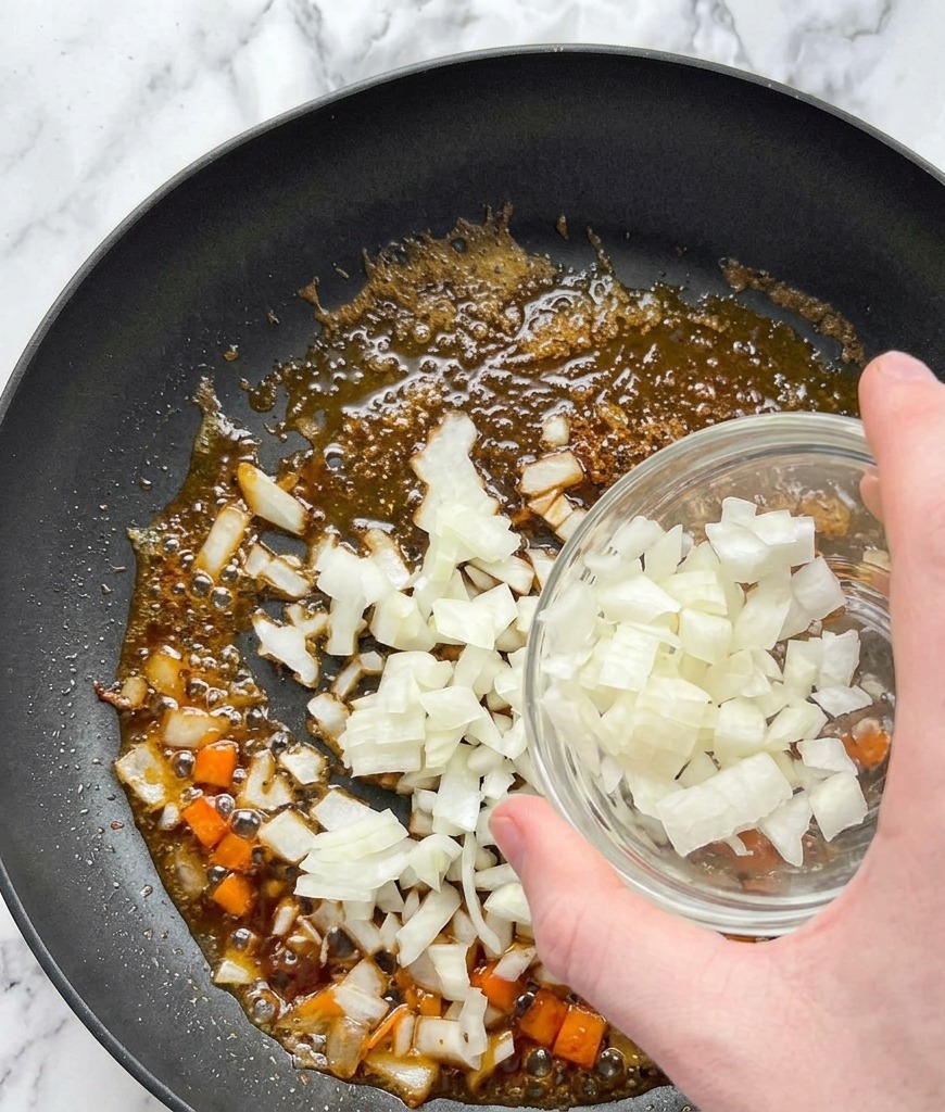 サーモンを焼いた後の旨味が残るフライパンに、ガラスのボウルからみじん切りの玉ねぎを入れている様子。