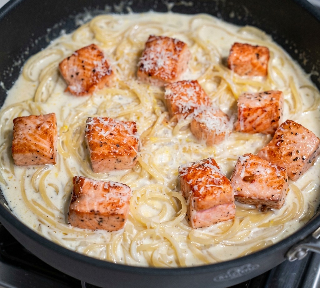 フライパンの中のサーモンとクリームパスタの上に、新鮮なパルミジャーノ・レッジャーノを細かく削りおろしている様子。