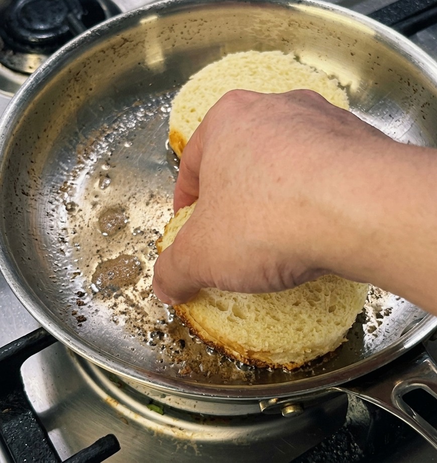 フライパンにのせた厚切りで丸い2枚のブリオッシュパンを、綺麗な焼き色をつけるために手で軽く押し当てている様子。