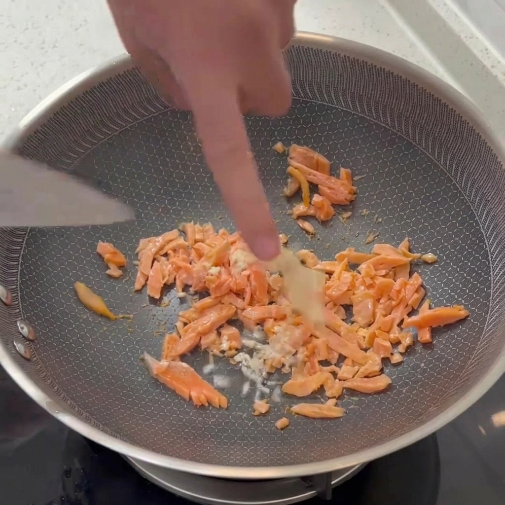 フライパンの中で、さっと炒めたスモークサーモンにみじん切りのにんにくをスパチュラで混ぜ合わせている様子。