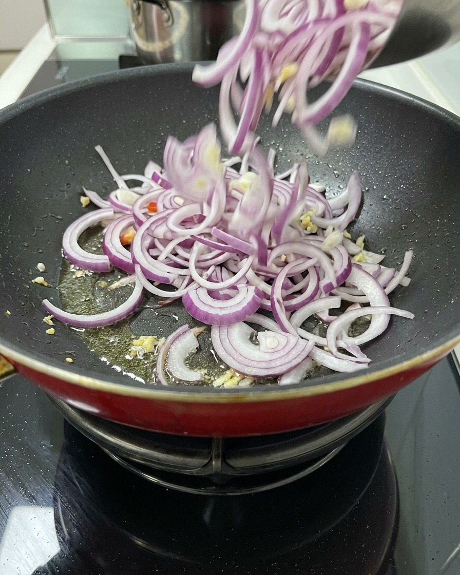 お肉を焼いた後のオイルと香味野菜が入ったフライパンに、ボウルから大量の刻んだ玉ねぎを投入して炒め始めるところ