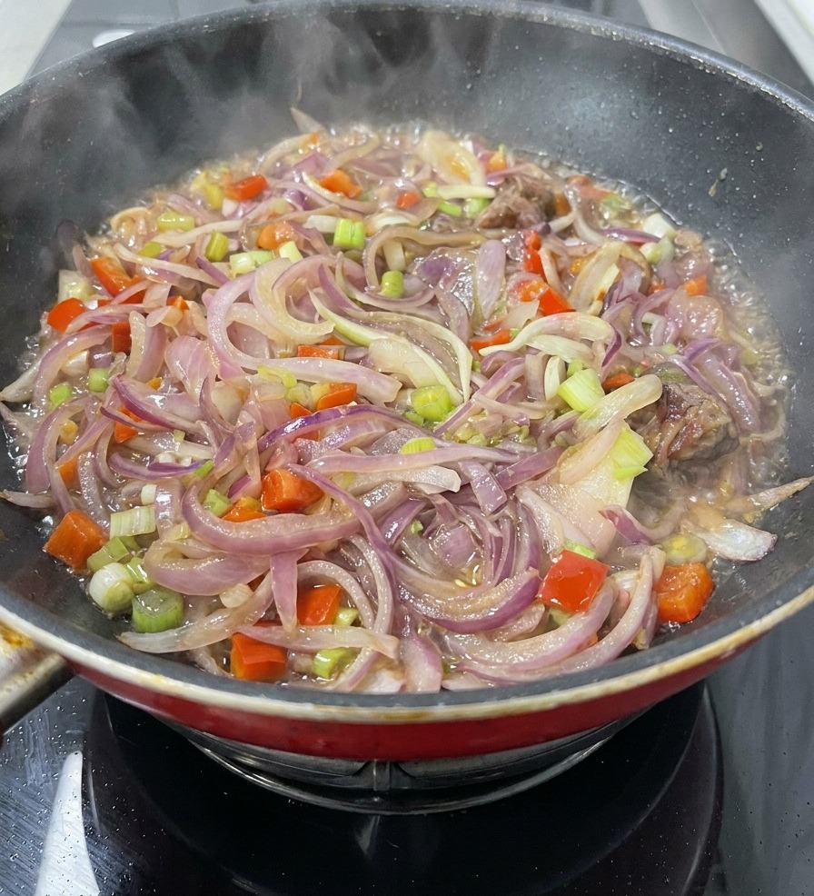 スライスした玉ねぎ、にんじん、セロリ、そしてお肉が軽い液体の中でコトコトと煮込まれ、湯気が上がっているフライパン