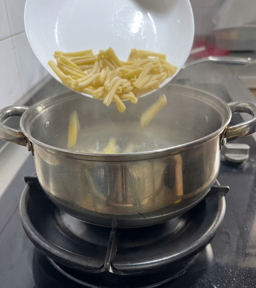 ガスコンロの上の鍋で沸騰したお湯の中に、白いお皿からカサレッチェパスタを投入している様子