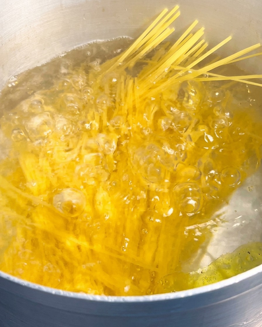 勢いよく沸騰した大きめの鍋のお湯の中に、乾燥した黄色いスパゲッティの束を沈めている様子。