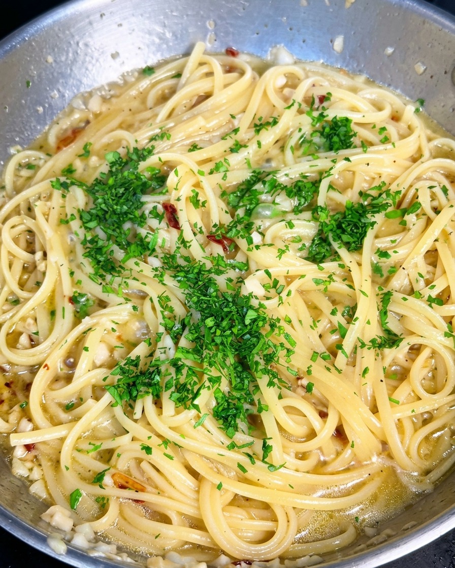 にんにくとオリーブオイルのパスタが入ったフライパン全体に、鮮やかな緑色の刻みパセリが散りばめられている様子。