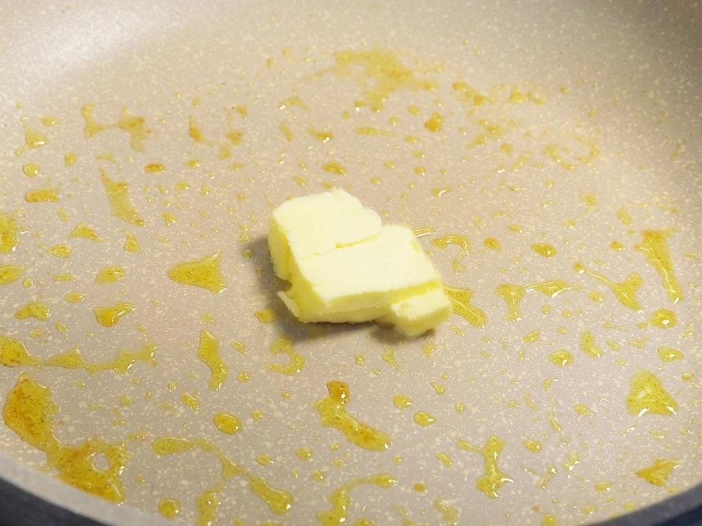 エビの旨味が残るフライパンの中で、四角い黄色いバターがじわじわと溶けている様子。
