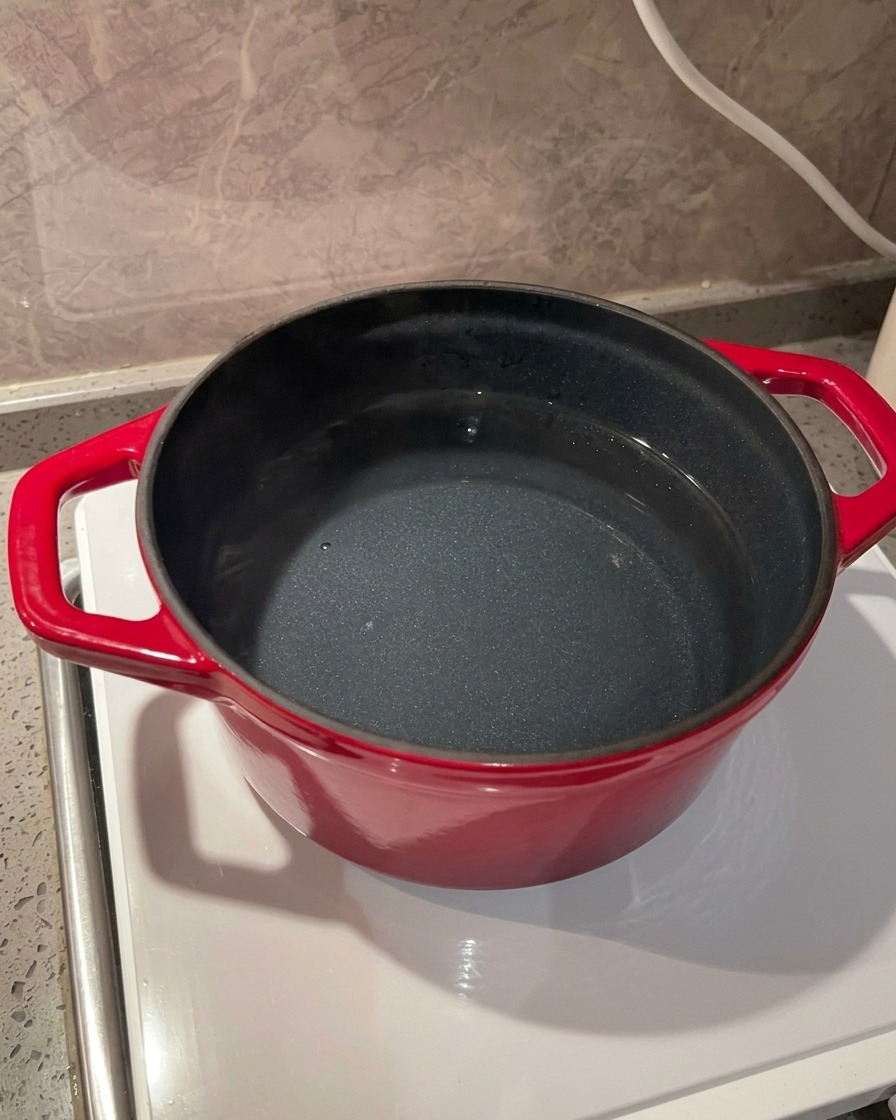 スタイリッシュなIHクッキングヒーターの上で、並々と水の入った鮮やかな赤色のお鍋に海塩を投入しているクローズアップ。