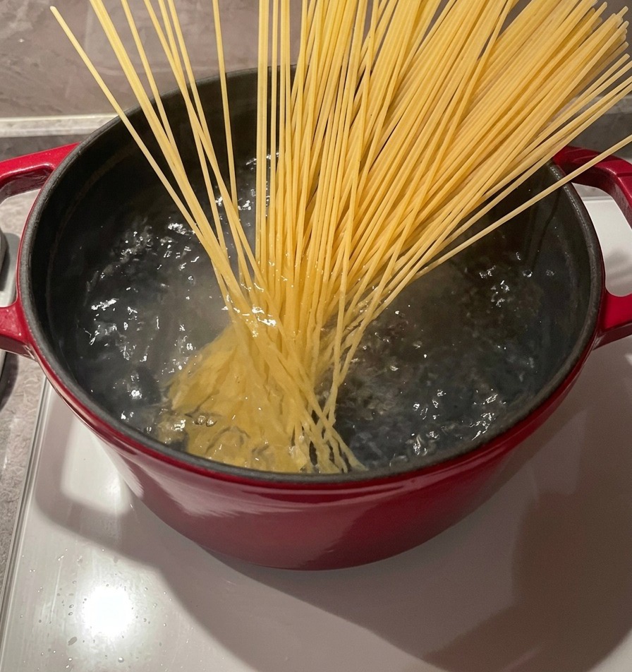 ぐつぐつと激しく沸騰するお湯が張られた鍋に、木製のお箸を使って乾燥スパゲッティの束を入れている様子。