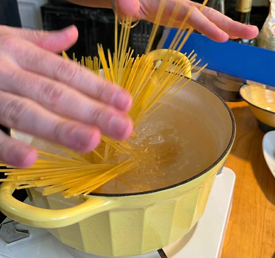 沸騰したお湯が入った黄色い鍋に、乾燥スパゲッティの束を入れている様子。