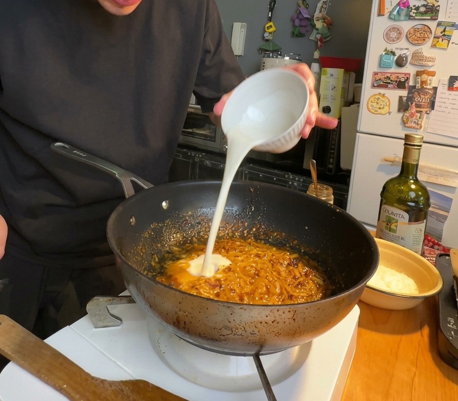 チリオイルと玉ねぎが入ってグツグツとしている赤みがかったソースベースに、生クリームを注いでいる様子。