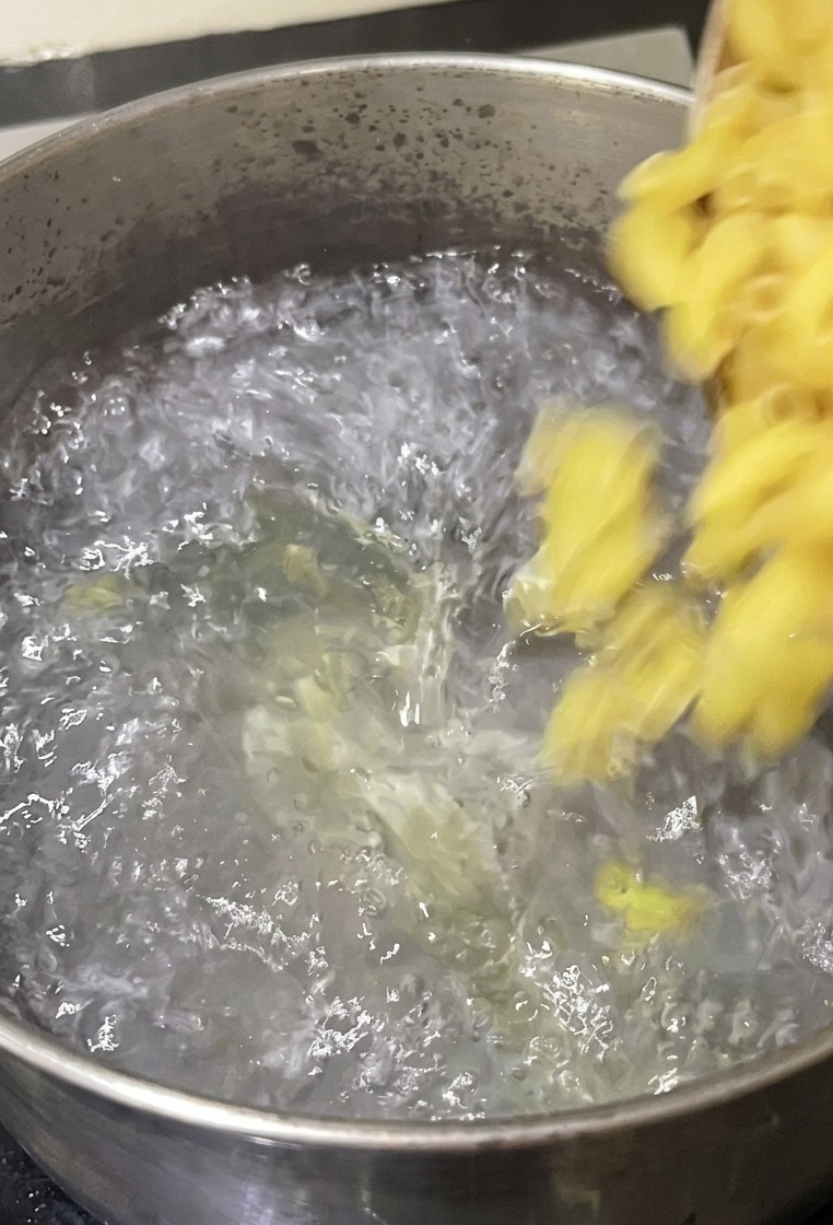鍋の沸騰したお湯の中に、ボウルからエルボーマカロニを入れている様子。