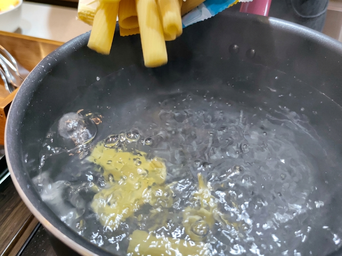 グラグラと沸騰したお湯がたっぷり入った鍋に、乾燥した黄色いリガトーニパスタを投入している様子