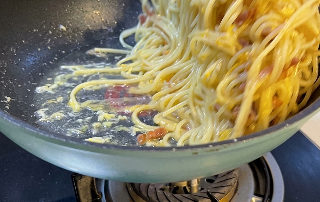 白いお皿に美しく盛り付けられたスパゲッティ・カルボナーラ。仕上げに削りたてのチーズと黒胡椒がトッピングされている様子。